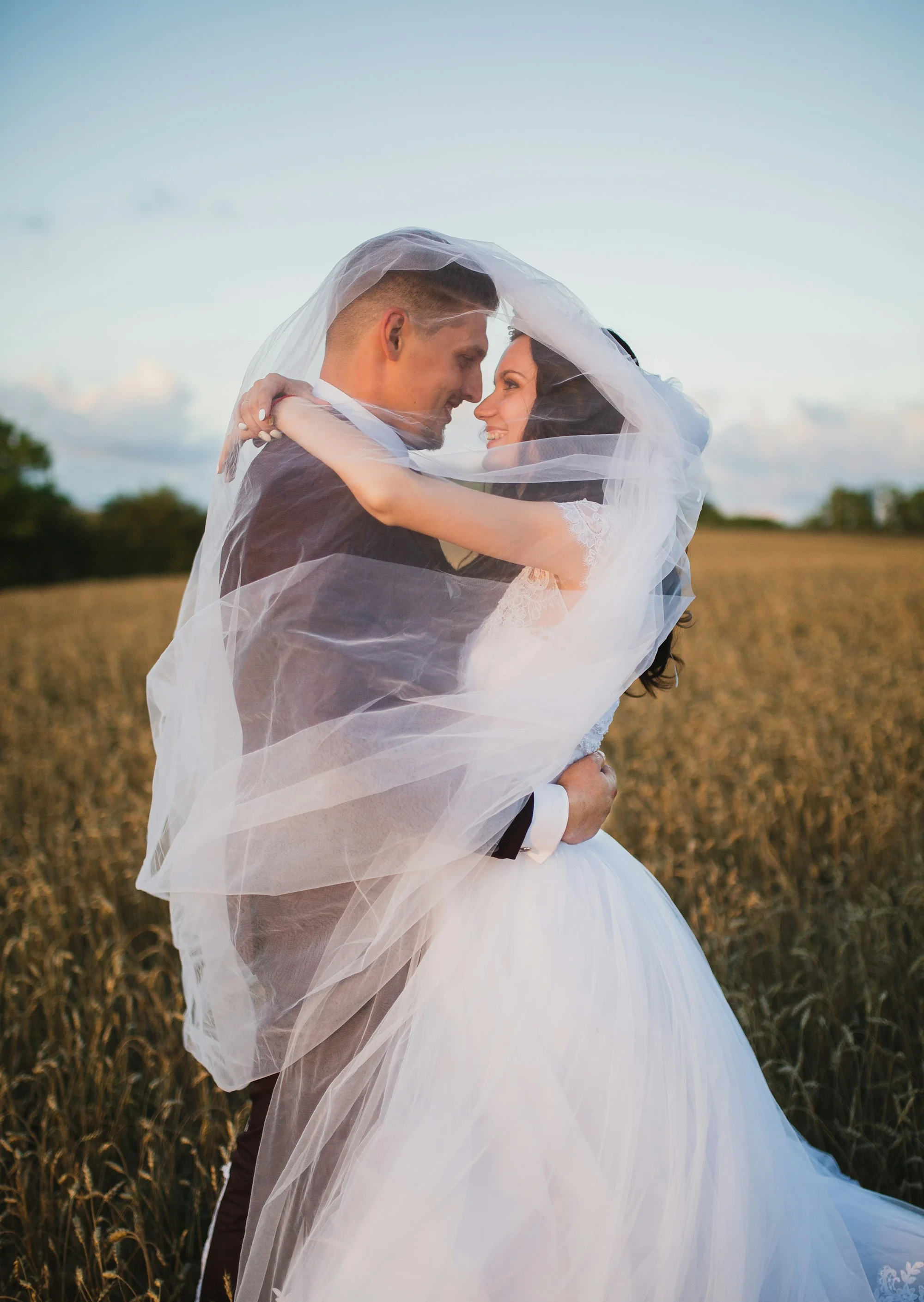 Lara and Stefan under a veil in a wheat field